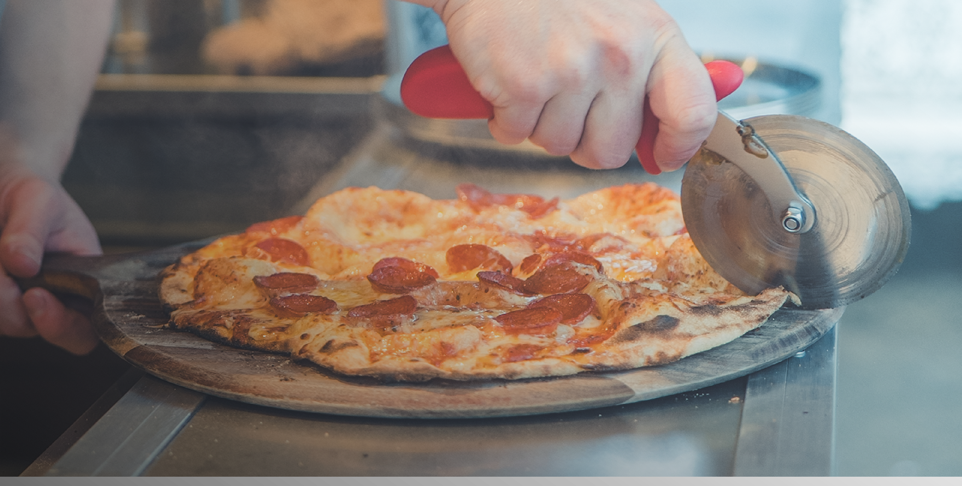 Pepperoni pizza being sliced with a pizza wheel